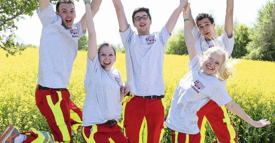 Jugendliche in Rettungsdienstkleidung springen gutgelaunt in die Höhe