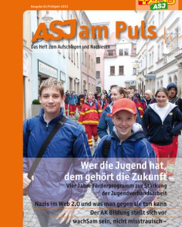 Titelseite des ASJ am Puls. Eine große Gruppe ASJlerinnen und ASJler läuft durch eine Stadt.